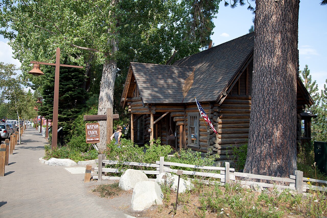 Watson Cabin’s log exterior and porch beside a large pine tree in Tahoe City